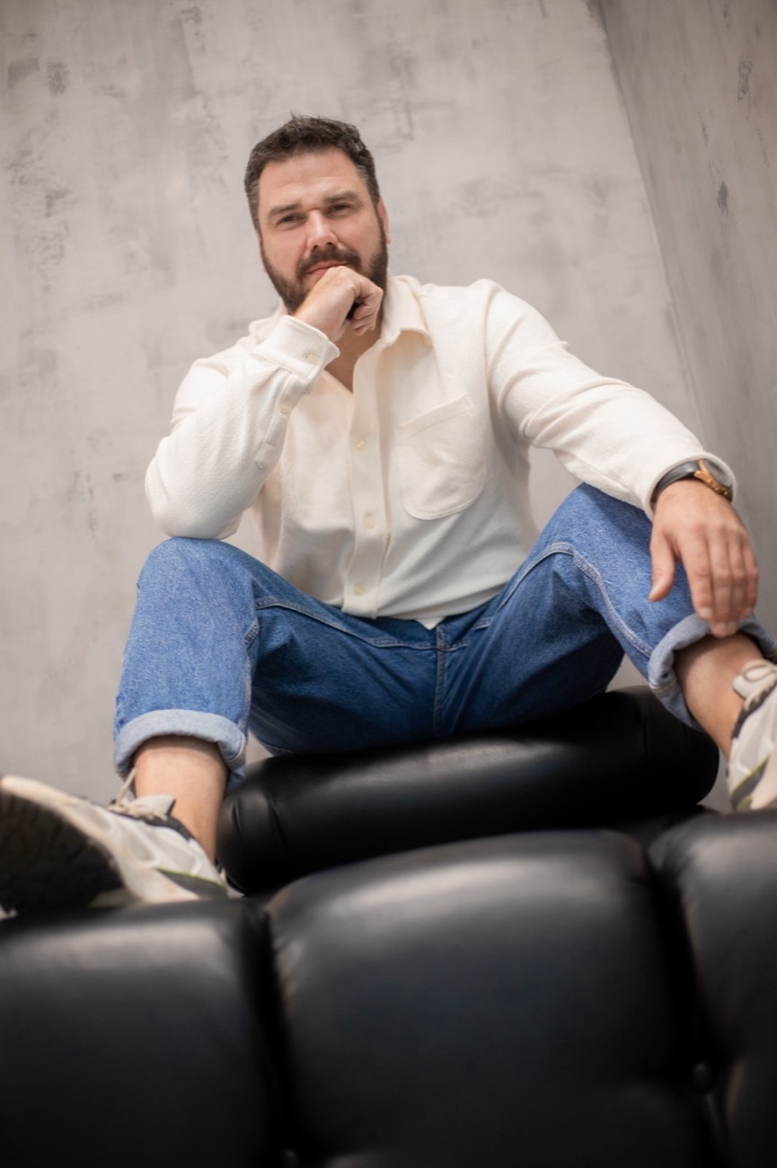 Bartosz Cibor – portret na siedząco w jasnej koszuli